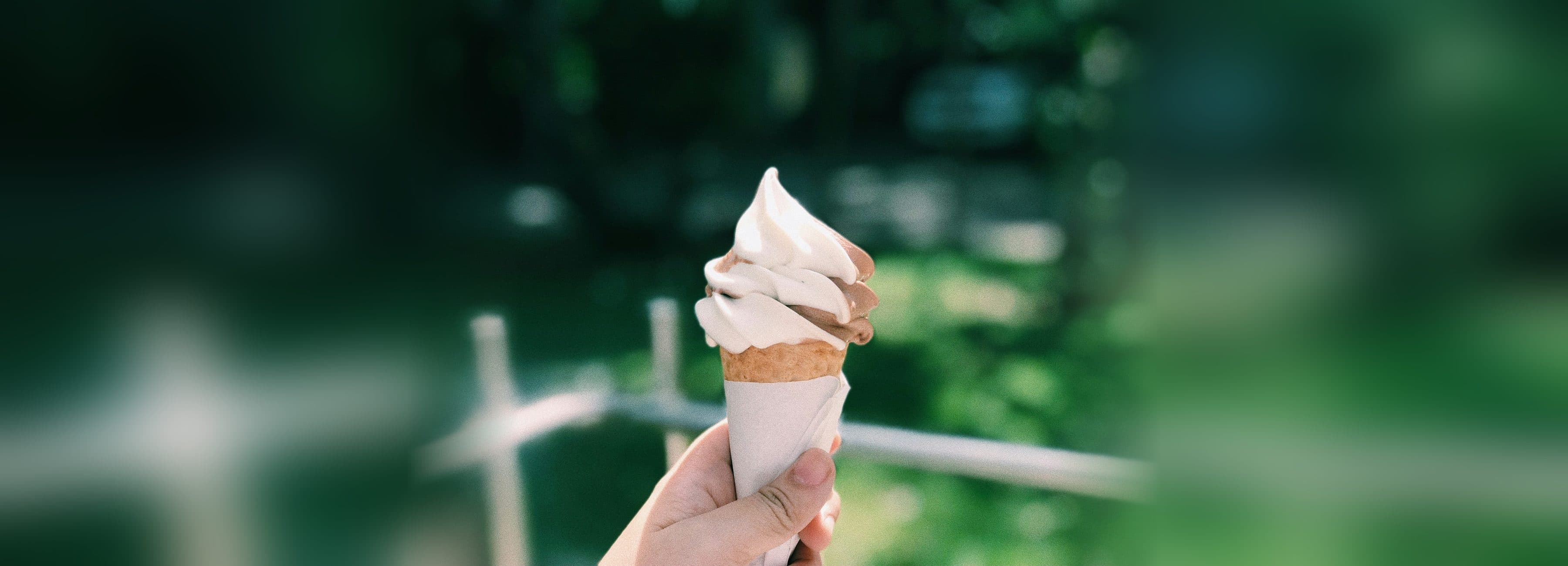 Softeis in der Waffel, gehalten vor sommerlich gruenem Hintergrund