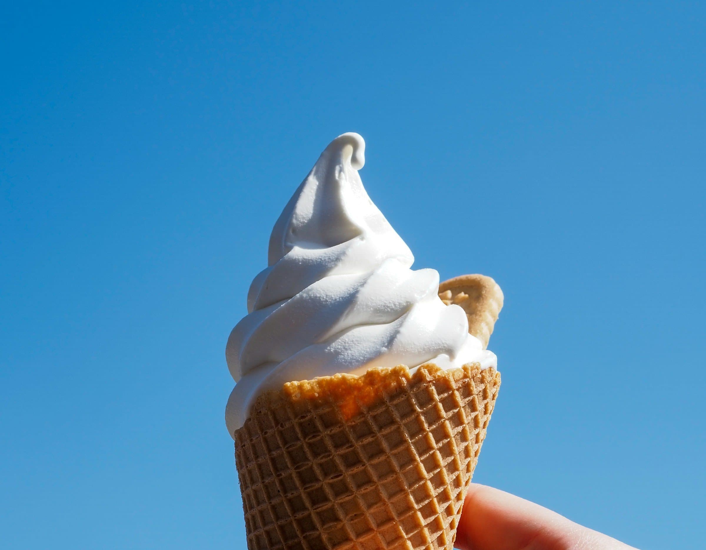 Frisch gezapftes Vanillesofteis in der Waffel vor strahlend blauem Sommerhimmel