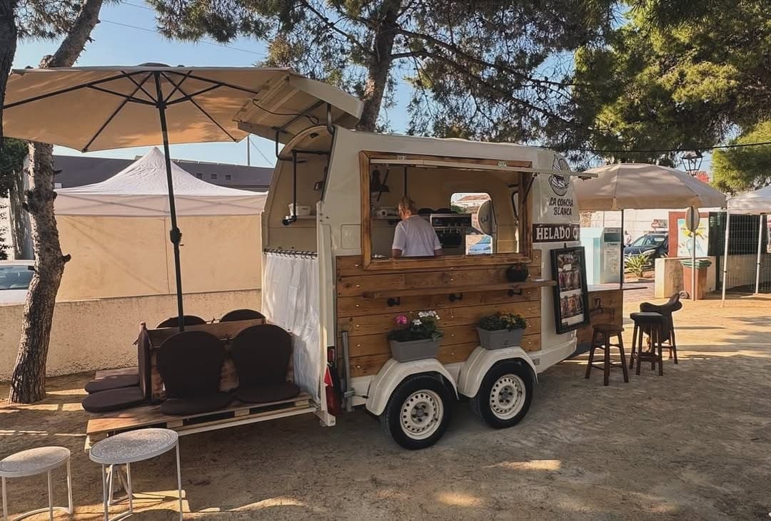 Softeis-Wagen mit Holztheke, Barhockern und Sonnenschirm auf einem Marktplatz